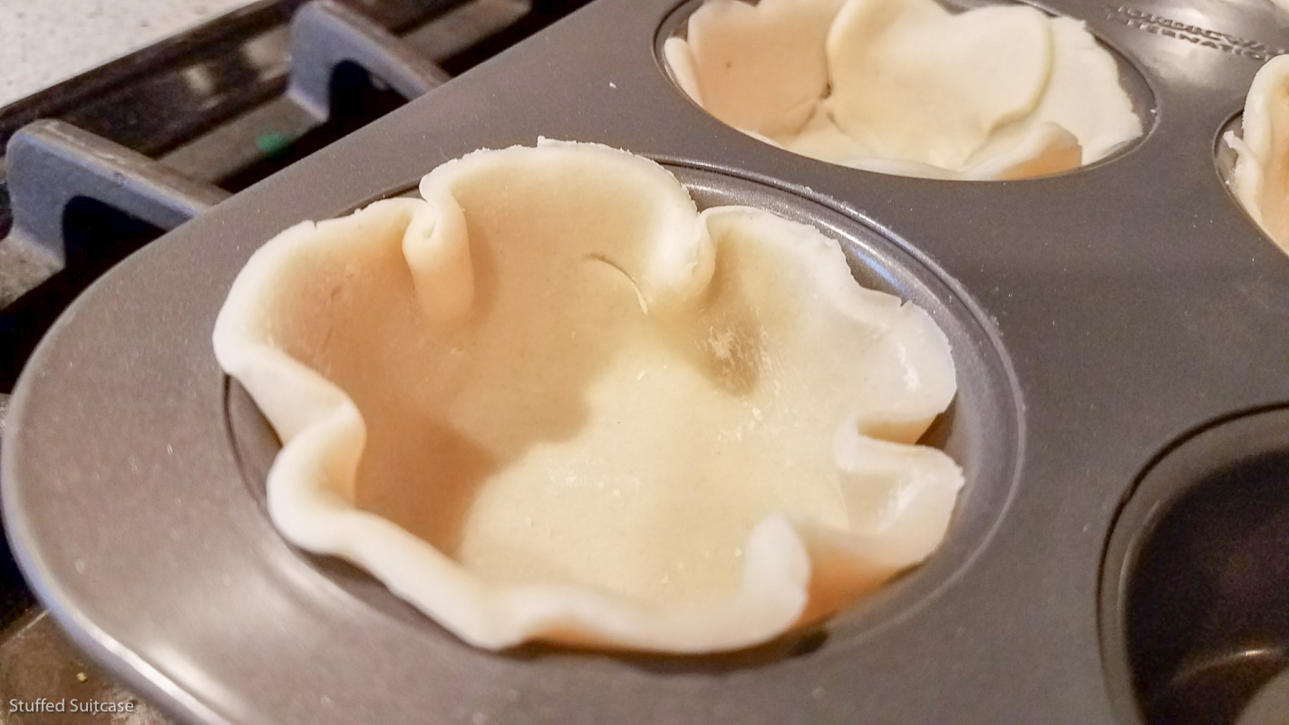 Cut pie crust into circles and place in cupcake pan © Stuffed Suitcase