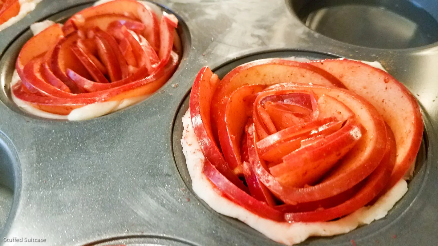 Roll cinnamon seasoned apple slices and place in cupcake pans to make rose apple pies © Stuffed Suitcase