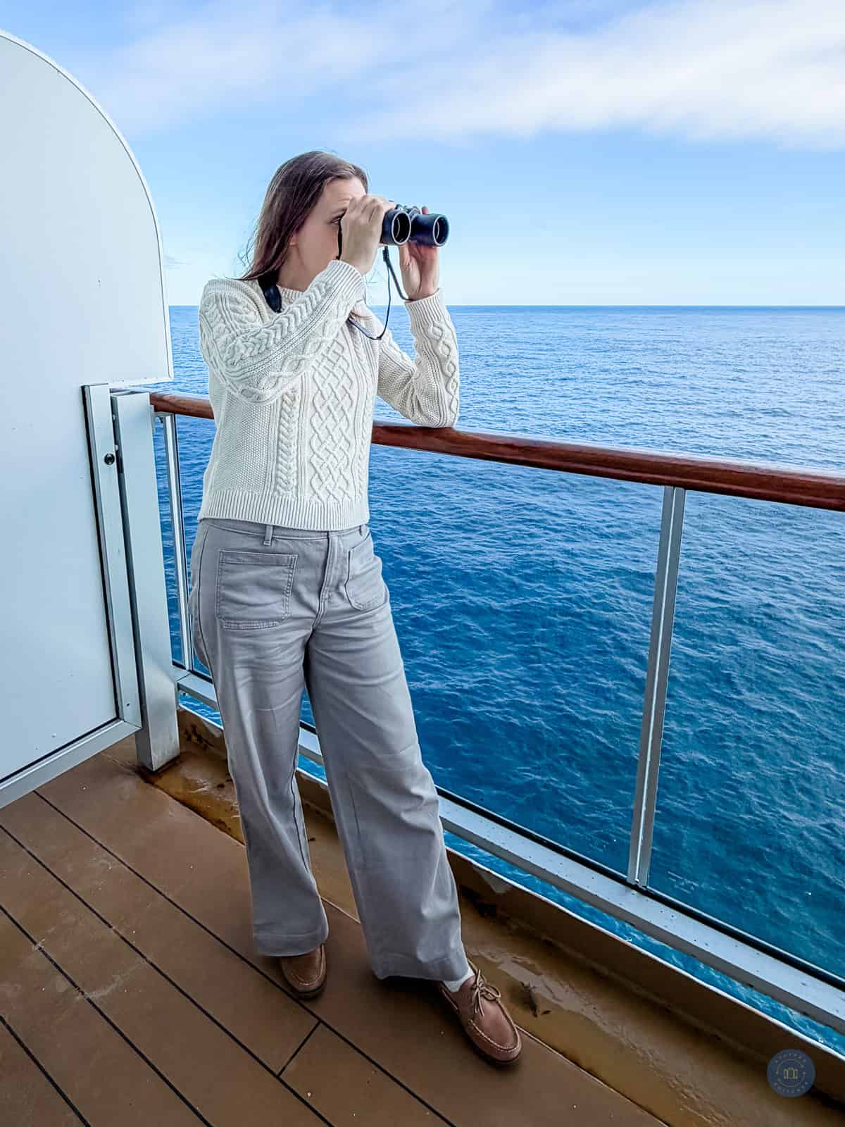 Woman using binoculars on alaska cruise ship balcony overlooking the ocean.
