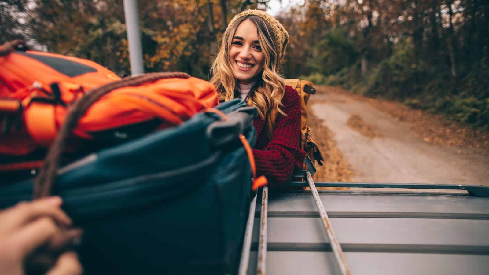 girl on road trip getting bag from roof of car