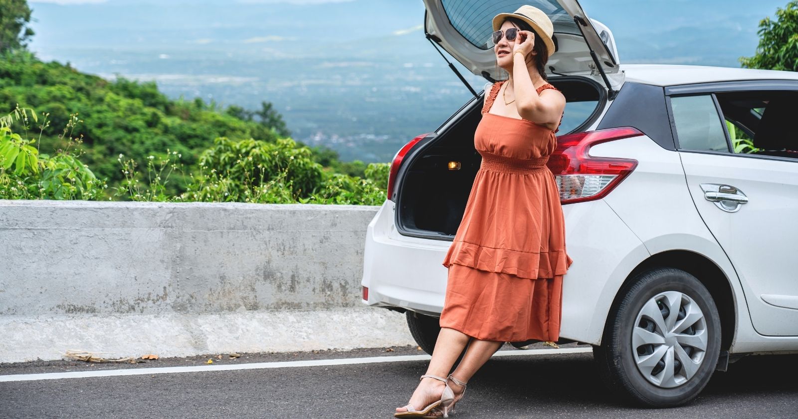 girl in dress next to car on road trip overlooking city