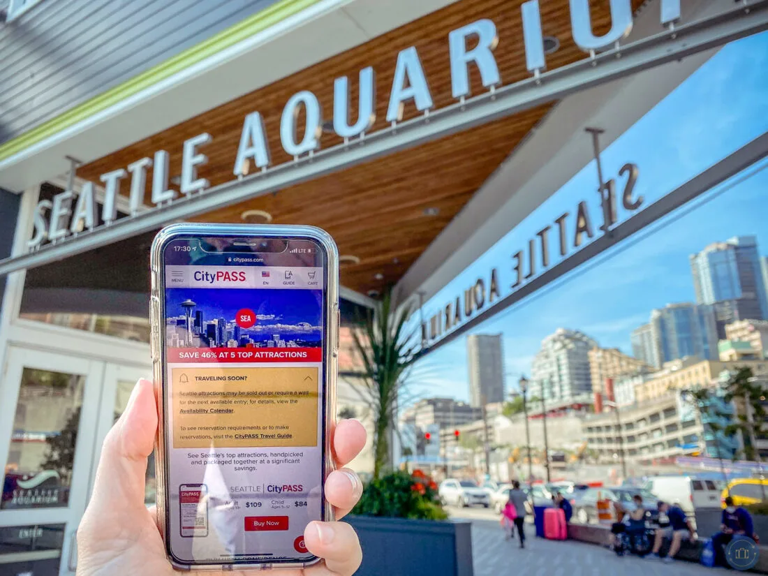 holding phone with citypass seattle screen in front of seattle aquarium entrance