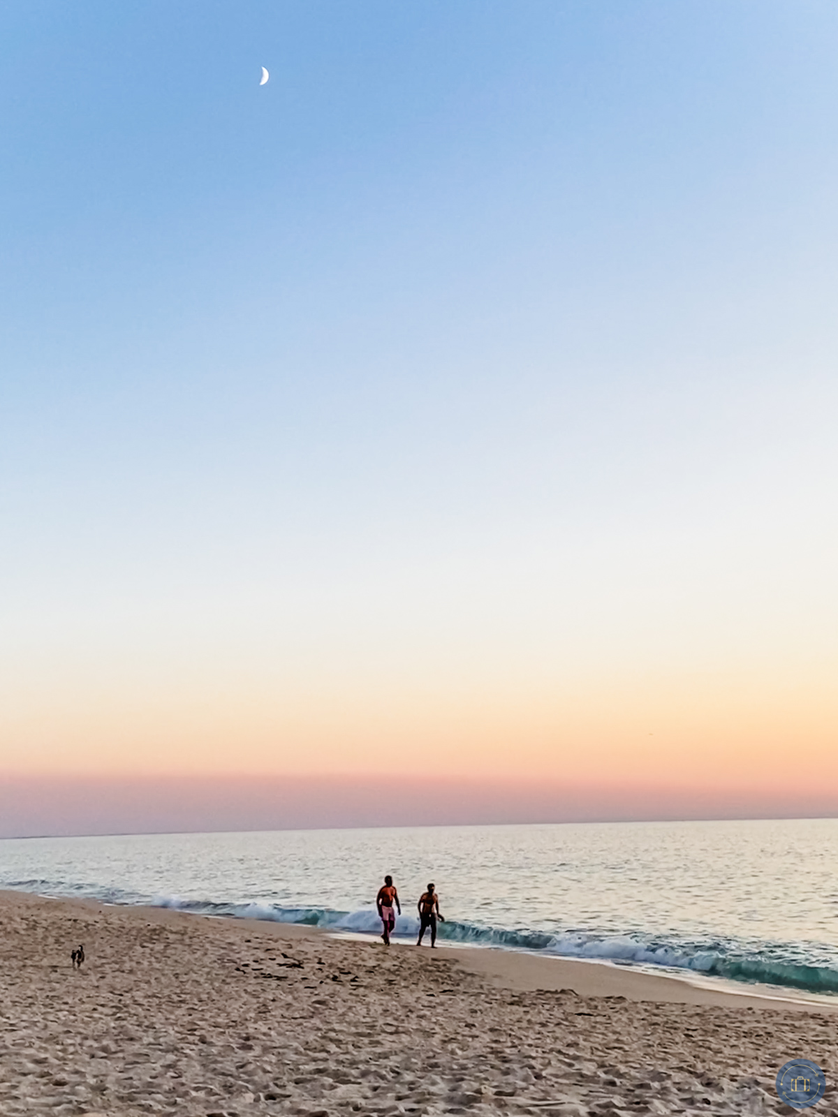 men walking on comporta beach in portugal at sunset with moon high in sky