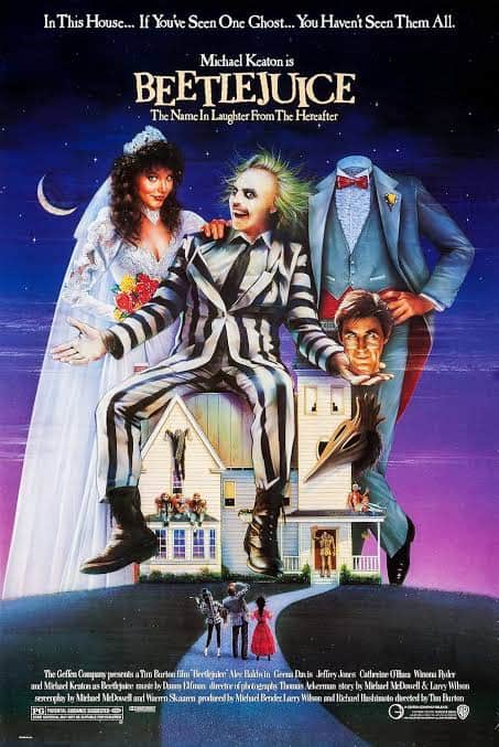 Michael Keaton as Betelgeuse in his striped suit sitting on top of a miniature model house alongside Geena Davis and Alec Baldwin for Tim Burton's Beetlejuice