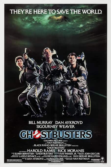 Bill Murray, Dan Aykroyd, and Harold Ramis standing shoulder-to-shoulder in flight suits and proton packs under a glowing green supernatural sky for a classic Ghostbusters feature