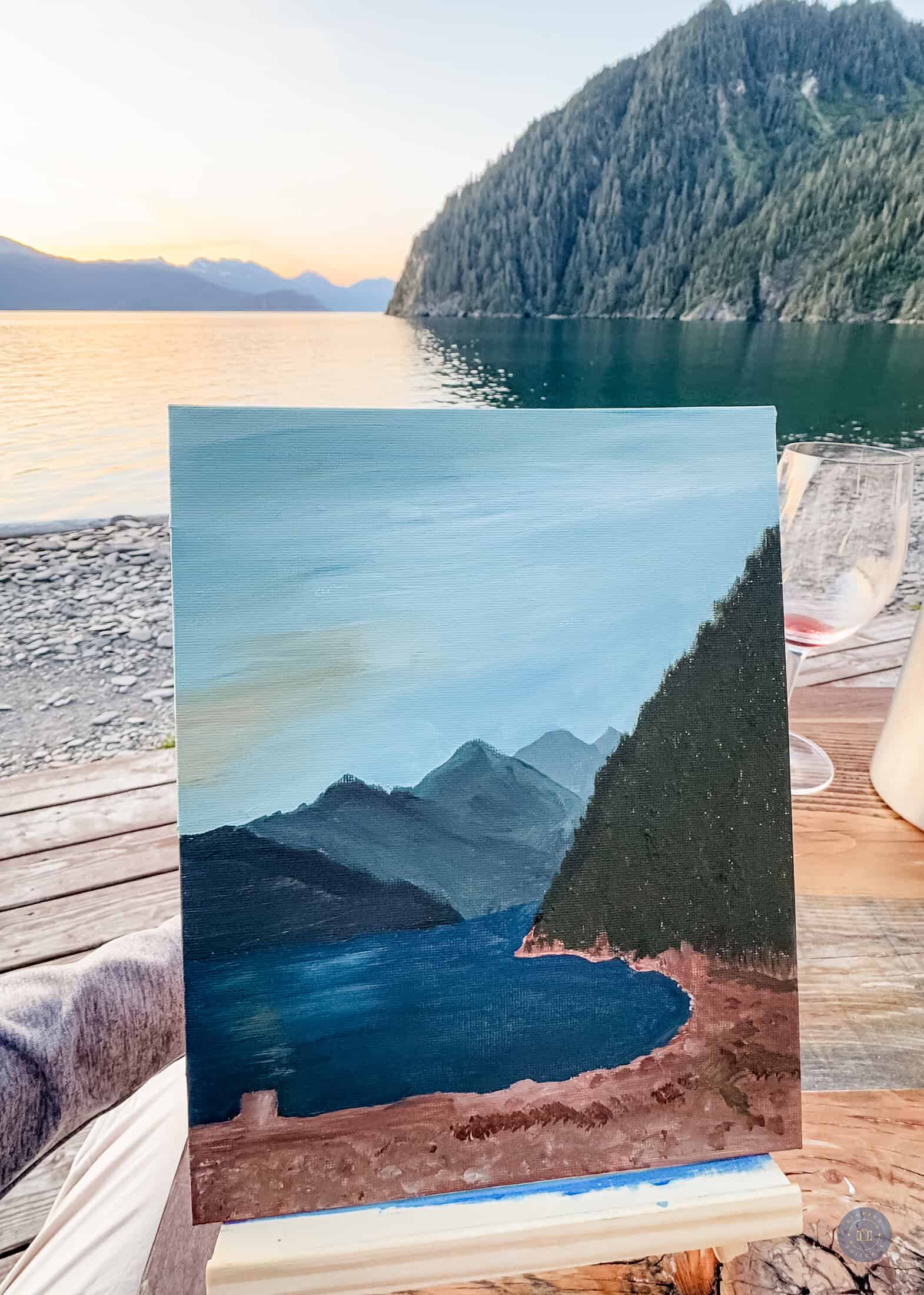 A painting of a lake and mountains at sunset.