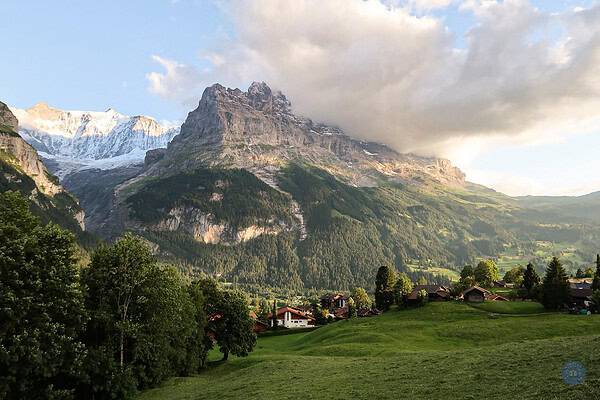 photo of the valley of Grindelwald Switzerland with small swiss houses in bottom of image and towering mountains of Eiger and Jungfrau