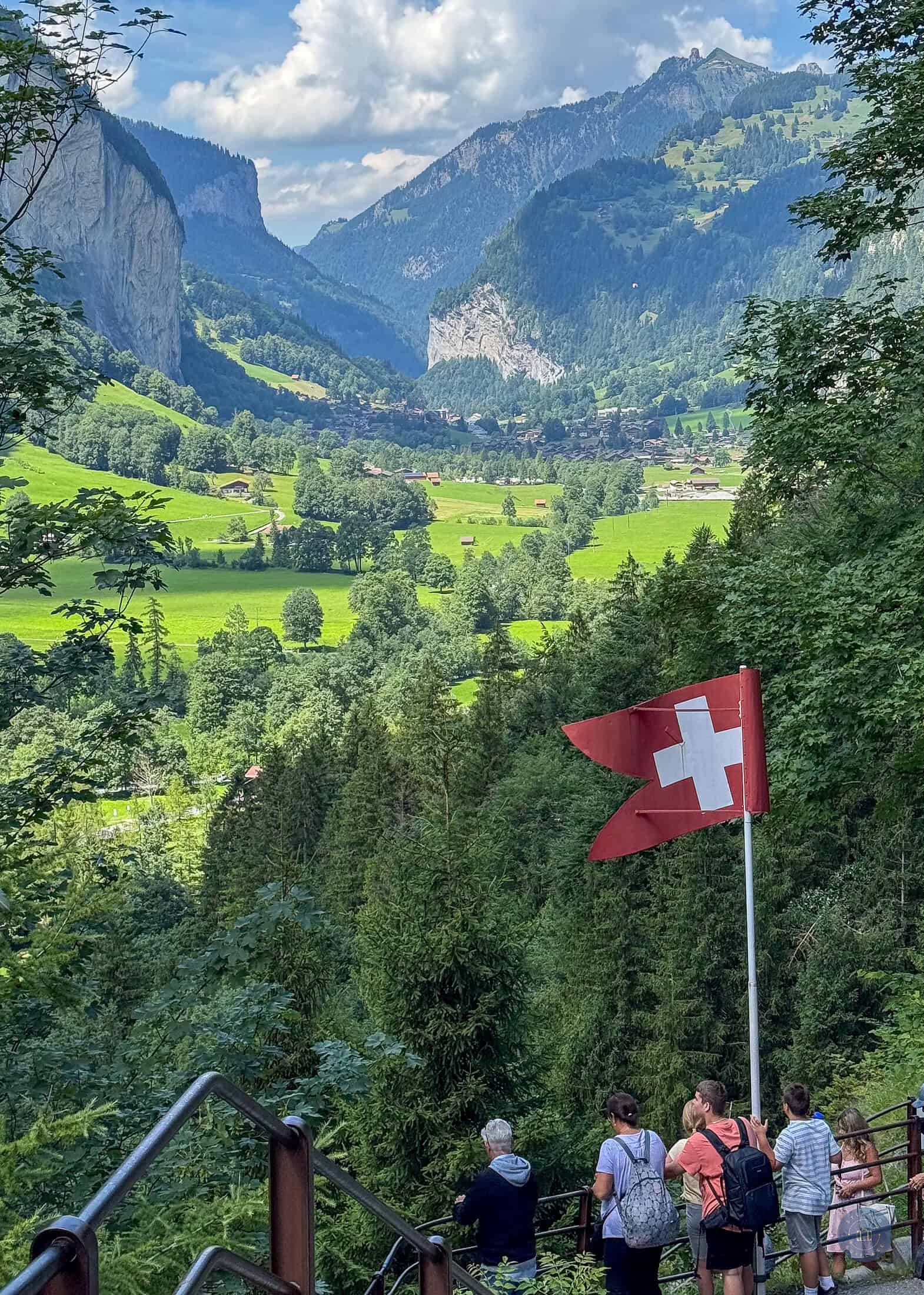 tourists standing by Switzerland flag overlooking the valley of Lauterbrunnen from Trümmelbach Waterfalls